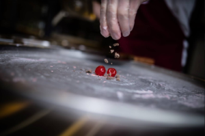 Person sprinkling chocolate chunks on maraschino cherries