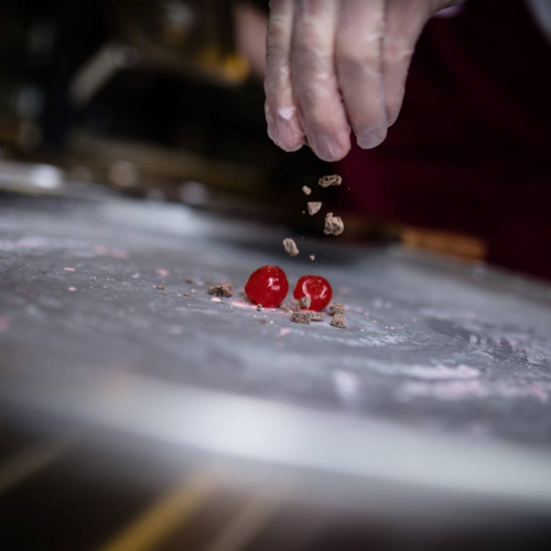 Person sprinkling chocolate chunks on maraschino cherries